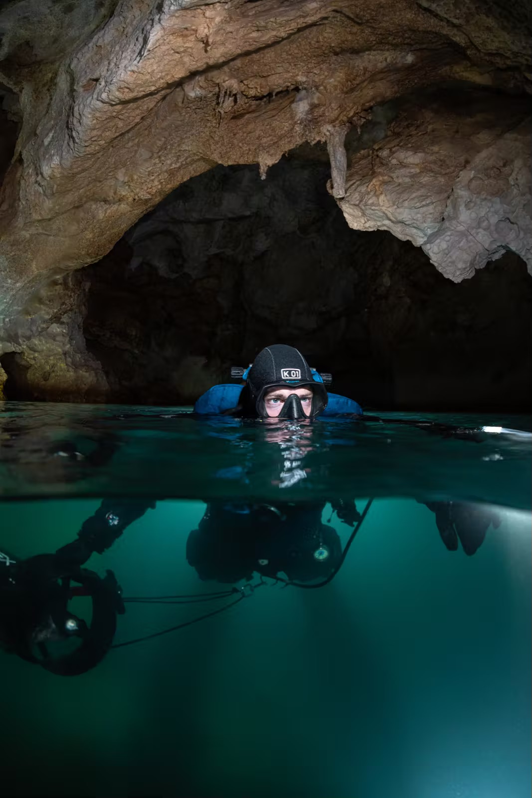 GUE cave diver split shot at cavern surface, half above half below water